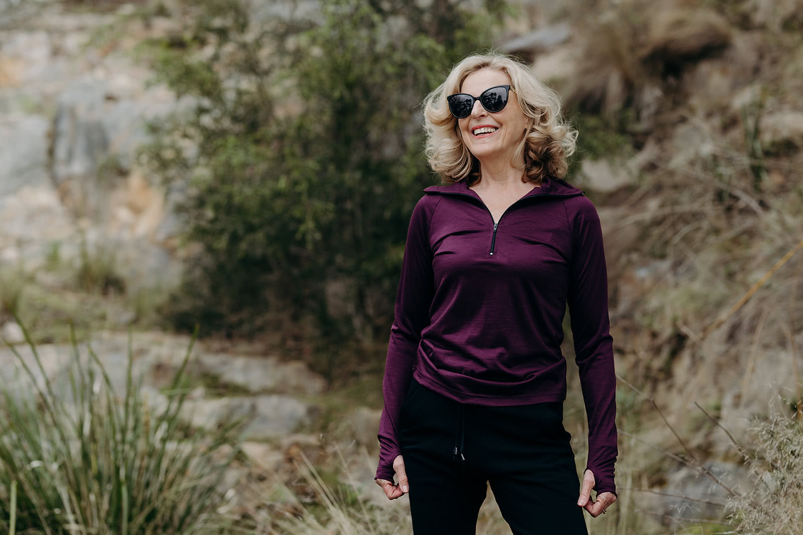 Woman wearing a purple long-sleeve shirt and sunglasses outdoors on a rocky trail.